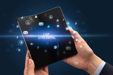 İş adamı elinde LIVE STREAMING yazıtlı, sosyal ağ kavramlı katlanabilir bir akıllı telefon tutuyor.