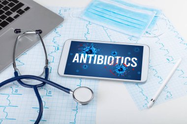 Beyaz yüzeyde ANTIBIOTICS yazıtları, salgın konsepti olan tablet pc ve doktor araçları