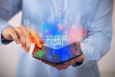 Öğrenci Kredisi ve eğitim konsepti içeren katlanabilir bir akıllı telefon tutan genç adam.