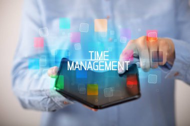 Time ManageMENT yazıtlı, eğitici konseptli katlanabilir bir akıllı telefon tutan genç adam.