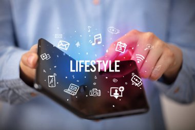 İş adamı, üzerinde LIFESTYLE yazıları ve sosyal medya kavramı olan katlanabilir bir akıllı telefon tutuyor.