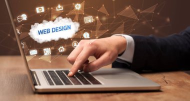 Web Tasarım yazıtları ve modern teknoloji konseptiyle birlikte dizüstü bilgisayarda çalışan bir işadamı.