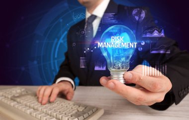 RISK MANAGEMENT yazıtları ve iş fikri kavramına sahip bir iş adamı elinde ampul tutuyor