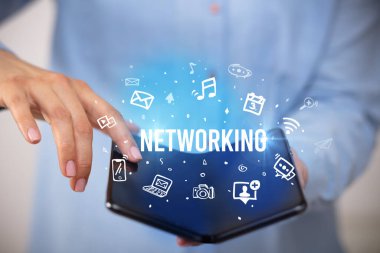 İş adamı elinde NETworking yazıtlı, sosyal medya kavramlı katlanabilir bir akıllı telefon tutuyor.