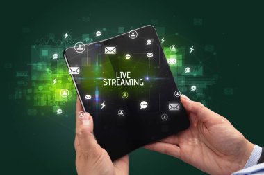 İş adamı elinde LIVE STREAMING yazıtlı, sosyal ağ kavramlı katlanabilir bir akıllı telefon tutuyor.