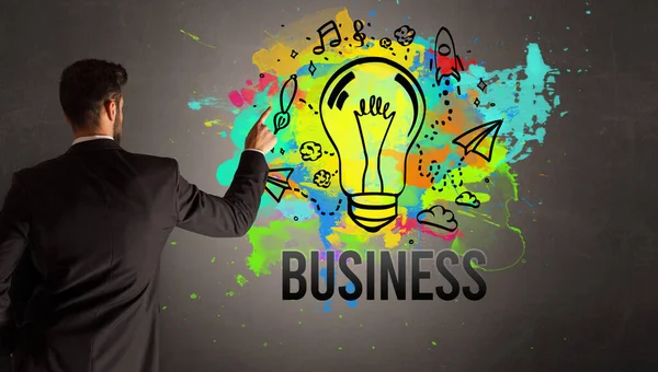 Businessman Drawing Colorful Light Bulb Business Inscription Textured Concrete Wall — Stock Photo, Image
