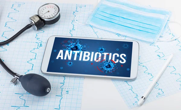 Beyaz yüzeyde ANTIBIOTICS yazıtları, salgın konsepti olan tablet pc ve doktor araçları