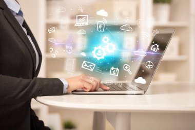 İş adamı dizüstü bilgisayarda çalışıyor, içinden dişli simgeleri çıkıyor, iş konsepti büyüyor.