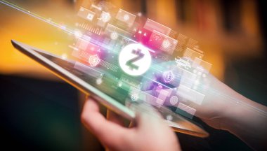 İçinden zcash simgeleri çıkan tablet kullanan bir elin yakın çekimi, dijital para birimi kavramı