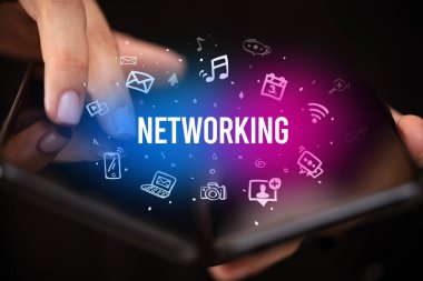 İş adamı elinde NETworking yazıtlı, sosyal medya kavramlı katlanabilir bir akıllı telefon tutuyor.