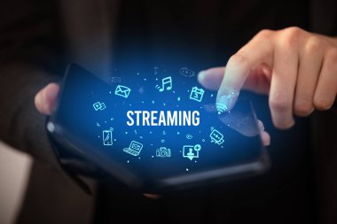 İş adamı elinde katlanabilir bir akıllı telefon tutuyor. Üzerinde STREAMING yazıtları ve sosyal medya kavramı var.