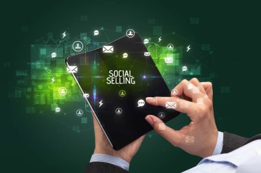 İş adamı elinde SOCIAL SELLING yazıtları, sosyal ağ konsepti içeren katlanabilir bir akıllı telefon tutuyor.