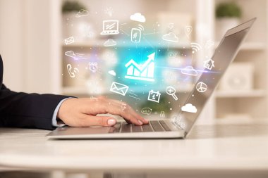 Dizüstü bilgisayarda çalışan iş adamı, içinden diyagram simgeleri çıkıyor, iş dünyası konsepti büyüyor.