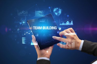 İş adamı takım oluşturma yazıtları ve başarılı iş konsepti içeren katlanabilir bir akıllı telefon tutuyor.