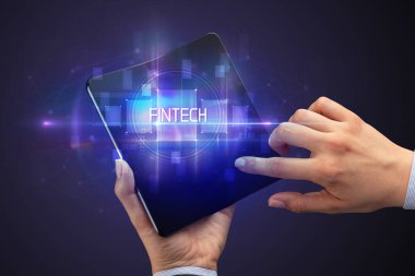 FINTECH yazıtları ve yeni teknoloji konsepti olan katlanabilir bir akıllı telefon tutan bir iş adamı