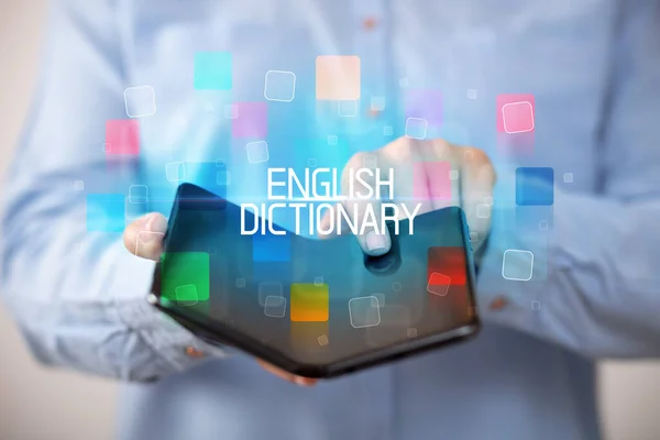 stock image Young man holding a foldable smartphone with ENGLISH DICTIONARY inscription, educational concept