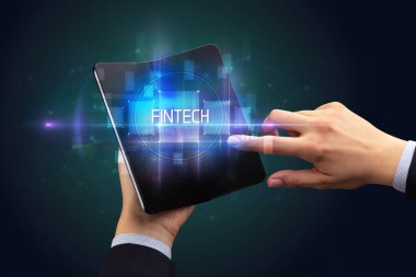 FINTECH yazıtları ve yeni teknoloji konsepti olan katlanabilir bir akıllı telefon tutan bir iş adamı