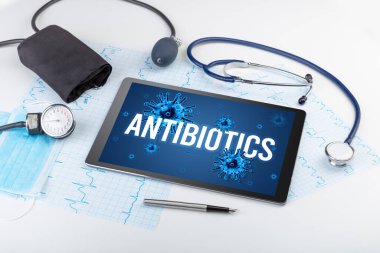 Beyaz yüzeyde ANTIBIOTICS yazıtları, salgın konsepti olan tablet pc ve doktor araçları
