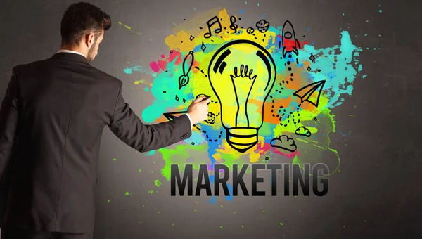テクスチャコンクリート壁にマーケティングの碑文とカラフルな電球を描くビジネスマン 新しいビジネスアイデアのコンセプト — ストック写真