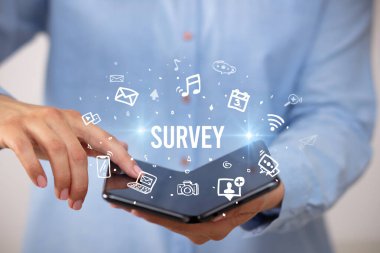 İş adamı elinde katlanabilir bir akıllı telefon tutuyor. Üzerinde SURVEY yazıları, sosyal medya kavramı var.