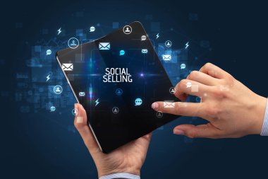 İş adamı elinde SOCIAL SELLING yazıtları, sosyal ağ konsepti içeren katlanabilir bir akıllı telefon tutuyor.