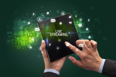İş adamı elinde LIVE STREAMING yazıtlı, sosyal ağ kavramlı katlanabilir bir akıllı telefon tutuyor.