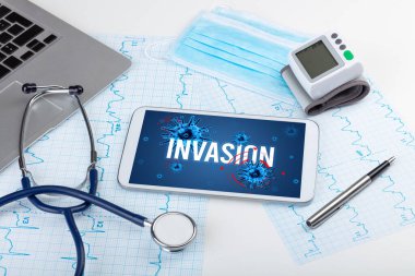 Beyaz yüzeyde INVASION yazıtları, salgın konsepti olan tablet pc ve doktor araçları