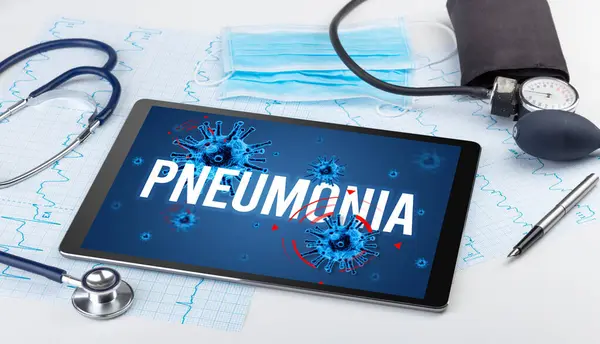 Tablet pc and doctor tools on white surface with PNEUMONIA inscription, pandemic concept