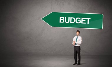 Bütçe yazıtları ve yeni iş yönü konseptiyle günlük bekleme yolu tabelasında genç iş adamı