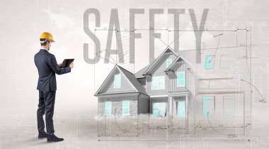 Güvenlik yazıtları ve ev planlama konseptiyle ilgili planları tutan genç bir mühendis.