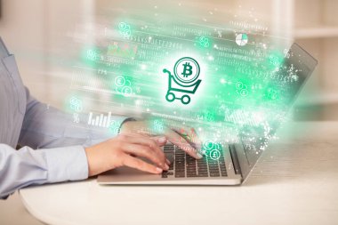 Bilgisayardan hisse senedi piyasasını izleyen genç bir adam. Üzerinde bitcoin simgeleri olan bir alışveriş arabası var.