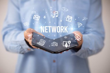 İş adamı elinde NETworK yazıtlı, sosyal medya kavramlı katlanabilir bir akıllı telefon tutuyor