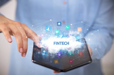 FINTECH yazıtlı, teknoloji konseptli katlanabilir bir akıllı telefon tutan bir iş adamı