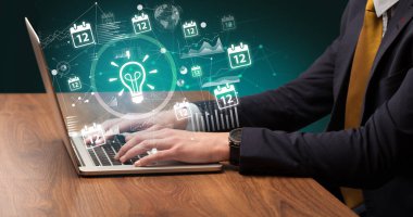 İş adamı ekrandan çıkan ampul simgeleriyle dizüstü bilgisayarda çalışıyor, başarılı iş konsepti