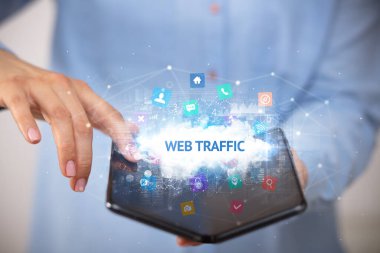 İş adamı elinde web trafiği yazıtlı, teknoloji konseptli katlanabilir bir akıllı telefon tutuyor.