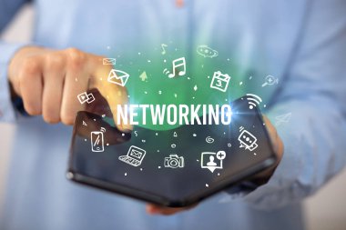 İş adamı elinde NETworking yazıtlı, sosyal medya kavramlı katlanabilir bir akıllı telefon tutuyor.