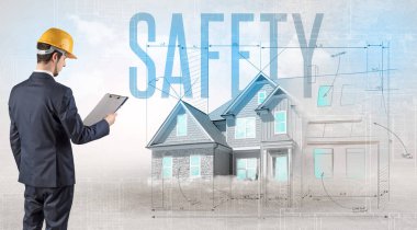 Güvenlik yazıtları ve ev planlama konseptiyle ilgili planları tutan genç bir mühendis.