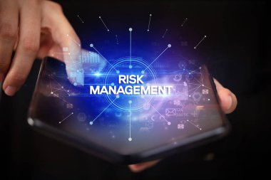 İş adamı, üzerinde Risk Yönetimi yazıtı ve yeni iş konsepti olan katlanabilir bir akıllı telefon tutuyor.