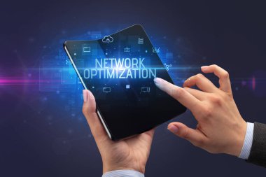 İş adamı elinde NETwork optimistasyon yazıtlı, siber güvenlik kavramına sahip katlanabilir bir akıllı telefon tutuyor.