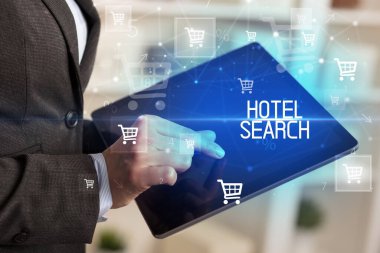 Genç kişi, HOTEL Arama yazısıyla online alışveriş uygulaması üzerinden alışveriş yapıyor