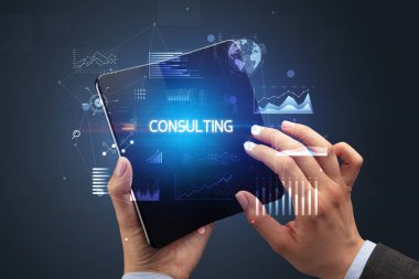 İş adamı katlanabilir bir akıllı telefon tutuyor. Üzerinde Danışmanlık yazısı ve başarılı bir iş konsepti var.