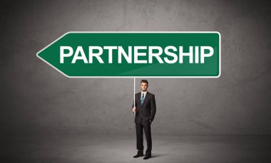 Genç iş adamı, üzerinde PARTNERGeIP yazıları ve yeni iş yönü konsepti olan günlük bekleme yolu tabelasında.