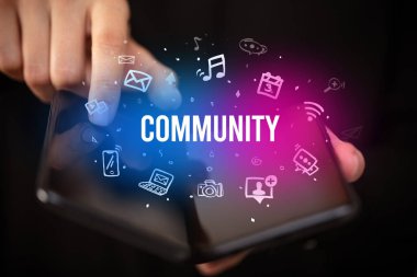 İş adamı, üzerinde COMUNITY yazıtları ve sosyal medya kavramı olan katlanabilir bir akıllı telefon tutuyor.