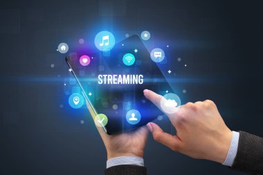 İş adamı elinde katlanabilir bir akıllı telefon tutuyor. Üzerinde STREAMING yazıtları ve sosyal medya kavramı var.