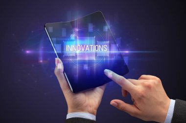 İş adamı elinde katlanabilir bir akıllı telefon tutuyor. Üzerinde InNOVATION yazıtları, yeni teknoloji konsepti var.