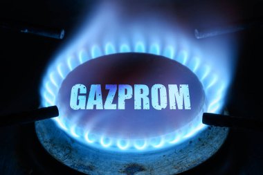 Gas burns in dark at home, blue fire flame and name Gazprom on stove ring burner. Concept of natural pipeline gas cost, warmth, energy crisis, economy, Russian Gazprom supply and Nord Stream 2.