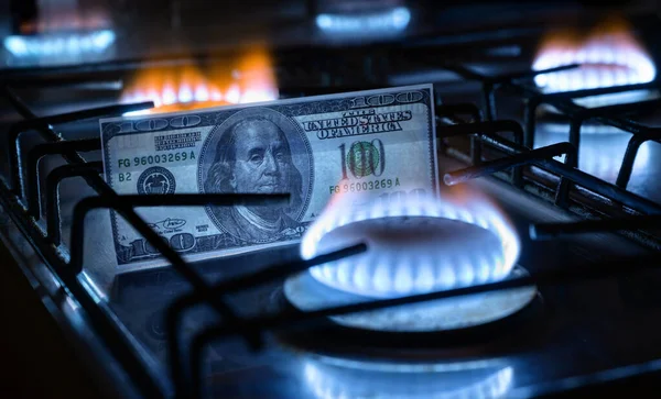 Gas burners and US dollar bill, USA money on home gas stove, blue propane flame and currency. Concept of World economy, energy crisis, oil, Russian natural gas cost, embargo and sanctions to Russia.
