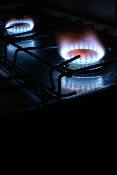 Gas stove at home, natural propane gas burns on dark background with black copy space, vertical view of blue fire flame of burners. Concept of gas cost, energy crisis, embargo, economy, Nord Stream.