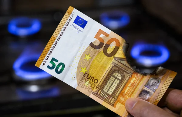 Euro money and gas burners, burnt EU banknote is by gas stove, European currency near blue propane flame. Concept of energy crisis in Europe, Gazprom, Germany, oil, natural gas cost, war, Nord Stream