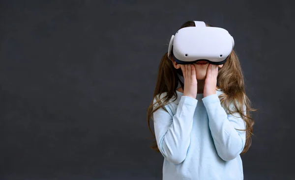Kid in metaverse, child uses virtual reality headset for new experience. Surprised little girl hands up to face looking in VR glasses, young person playing video games. Background, education concept